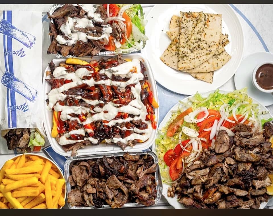Trays of charcoal meat, chips, salad and pita laid out for a group