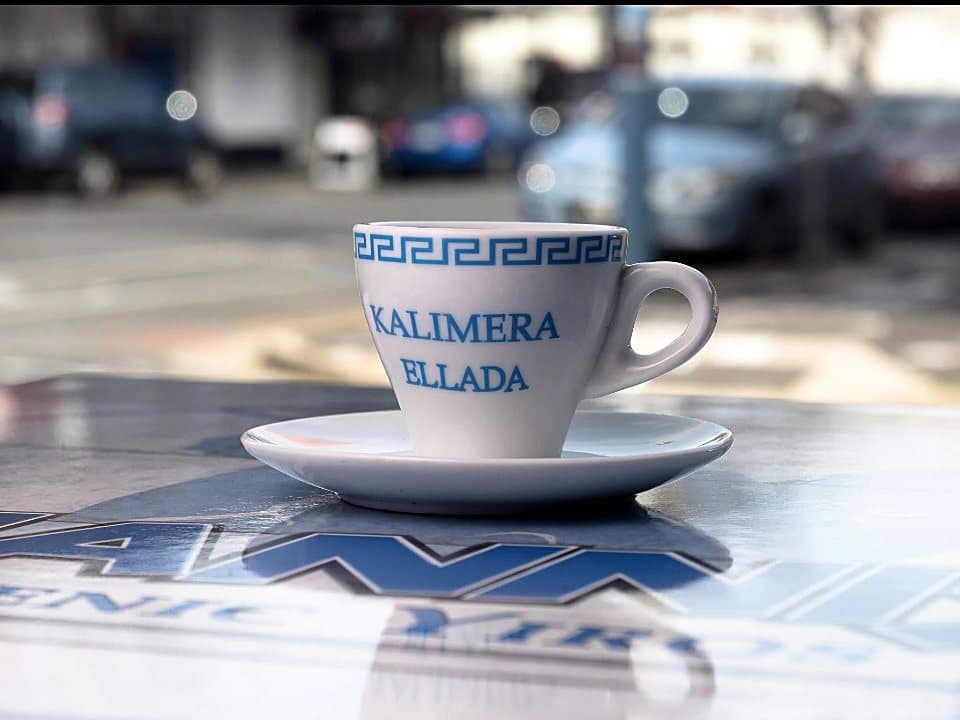 A Greek coffee in a meander-patterned cup reading Kalimera Ellada